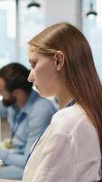 Vertical Junior dev developing software applications, optimizing code for performance, listening music. Young female engineer wearing headphones in office using AI to resolve bottlenecks, camera A video