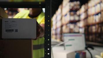 Fulfillment center staff engages in airway bills scanning for order tracking, using scanner on shipping labels in the warehouse. Worker wearing hi vis vest in storage room with shelves. Camera A. video