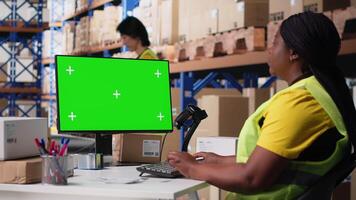 negro hembra trabajador gestiona pedidos siguiente a verde pantalla mostrar, exhibiendo almacén automatización herramientas y inventario controlar tableros de instrumentos. comercio electrónico orden Procesando con almacenamiento bastidores cámara b. video