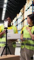Vertical Multiethnic employees promoting the merchandise in boxes on a , live streaming a vlog near industrial storage racks in the storehouse. Large business promotional advertisement. Camera A. video