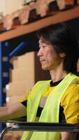 Vertical Asian man wheelchair user typing tracking numbers on a computer software, updating parcel status in real time. Staff managing order fulfillment in a logistics center to sort inventory. Camera B. video