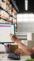 Vertical Asian employee typing tracking info from airway bill labels before shipping parcels, managing the order fulfillment process in industrial storehouse. Large business depot with packages Camera A. video