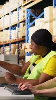 Vertical African american and asian workers reviewing shipment route and details for the real time parcel tracking info on computer software, managing order fulfillment in a logistics center. Camera A. video