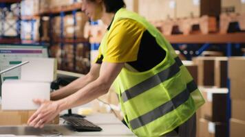 Asian employee using scanner to register shipping labels on cardboard boxes, professional tracking software to ensure express delivery. Online shopping large business tasks. Camera B. video