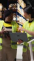 Vertical Multiethnic team in hi vis vests managing retail business operations, doing product handling from the warehouse big racks. Colleagues overseeing import export activity. Camera A. video