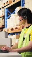 Vertical Call center male worker answer help line calls in a logistics warehouse, updating clients on orders and resolving cargo mix ups. Managing shipping software and airway bills. Camera A. video