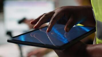 Close up of black woman monitoring e-commerce activity on tablet, preparing orders before shipment in industrial warehouse space. Employee managing the storehouse merchandise. Camera A. video