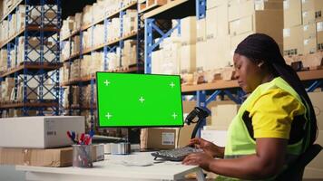 svart kvinna arbetstagare förvaltar order Nästa till grön skärm visa, visa upp lager automatisering verktyg och lager kontrollera instrumentpaneler. e-handel beställa bearbetning med lagring ställ. kamera a. video