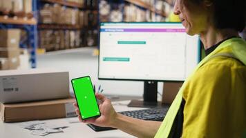 Storehouse worker in hi vis vest uses chroma key display on phone for shipping software management, packaging systems and inventory management tools. E-commerce logistics. Camera A. video