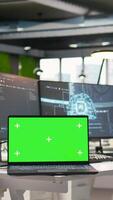 Vertical Chroma key notebook in AI industry startup workspace leveraging machine learning technology. Empty startup office with isolated screen laptop and artificial intelligence program running on monitors video