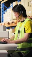 Vertical E-commerce support clerk responding to problems like lost parcels or order tracking, surrounded by cargo boxes on racks in a distribution hub. Call center operations on headset. Camera A. video