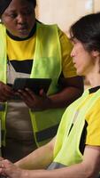 Vertical Depot coworkers processing orders and preparing the packages together, retail distribution in industrial logistics center. Team wearing hi vis vests surrounded by storage racks. Camera B. video