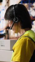 Vertical E-commerce support clerk responding to problems like lost parcels or order tracking, surrounded by cargo boxes on racks in a distribution hub. Call center operations on headset. Camera B. video