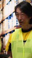 Vertical African american and asian team prepare shipments for dispatch with digital inventory and cargo pallets on depot racks. Working in a large scale distribution hub for express delivery. Camera B. video