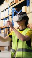 Vertical Employee uses virtual reality glasses to improve e-commerce operations, examining inventory goods and monitoring parcel status on package tracking software. VR headset technology. Camera A. video