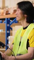Vertical Asian employee registering airway bills in storehouse industrial depot, scanning barcode for shipment details on the package tracking software. Fulfillment center inventory tracking. Camera B. video