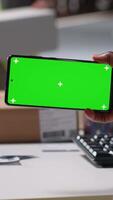 Vertical Staff reviews green screen pc in the storage room for data entry, inventory tracking mockups and visuals or barcode printer interfaces. Logistics worker packages cargo in the foreground. Camera B. video