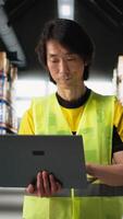 Vertical Asian male employee oversees product handling and order fulfillment, ensures inventory control using technology and packages coordination for efficient local delivery service. Camera B. video