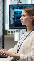 Vertical Female technician coding with AI language model assistance in startup office, using PC. Intern using computer, integrating artificial intelligence LLM assistant suggestions into code editor, camera A video