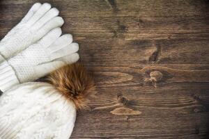 Wooden background with warm white gloves and hat with pom pom. Winter mood, copy space. photo