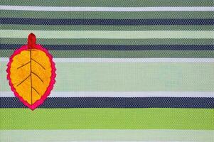 Yellow leaf handmade of fabric on striped background with copy space photo