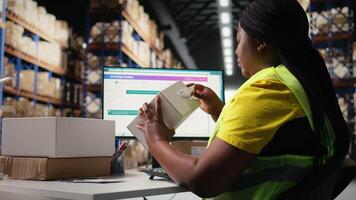 African american staff works on packages labeling for express delivery, ensuring accurate package tracking with a professional software. Worker processing orders in stock room. Camera A. video