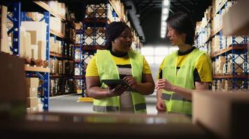 afrikansk amerikan och asiatisk team förbereda transporter för avsändande med digital lager och frakt pallar på depå ställ. arbetssätt i en stor skala distribution nav för uttrycka leverans. kamera a. video