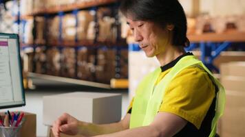 Asian staff manages awb labeling and scanning barcodes before dispatch, wearing hi vis vest in a warehouse for retail distribution. Ensuring order fulfillment and inventory tracking. Camera B. video