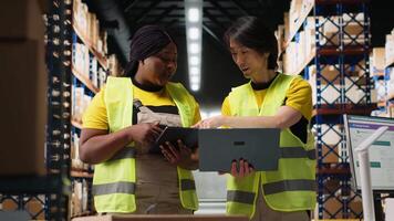 Team of diverse workers handling tracking software for parcel status on tablet, following the cargo shipment from the industrial warehouse with racks. Staff in hi vis vests. Camera B. video