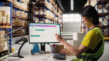 Asian employee typing tracking info from airway bill labels before shipping parcels, managing the order fulfillment process in industrial storehouse. Large business depot with packages Camera A. video