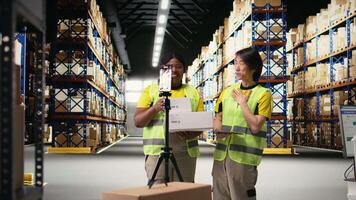 Multiethnic employees promoting the merchandise in boxes on a , live streaming a vlog near industrial storage racks in the storehouse. Large business promotional advertisement. Camera A. video