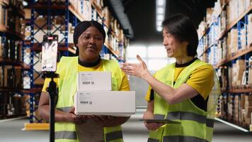African american and asian team presenting the cargo goods on a live stream , recording a vlog in industrial warehouse near racks. Content for large business advertisement. Camera B. video