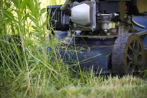 Close-Up View of Lawn Mower Cutting Overgrown Grass in Summertime photo