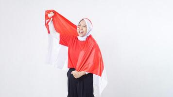 Beautiful Asian girl celebrate Indonesia independence day in red and white outfit showing patriotic pose with Indonesian flag draped around her back like a cape isolated on white background photo