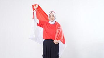 Beautiful Asian girl celebrate Indonesia independence day in red and white outfit showing victory pose with Indonesian flag draped around her back like a cape isolated on white background photo