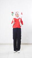 Beautiful Asian girl celebrate Indonesia independence day in red and white outfit holding a rose and tiny Indonesia flag isolated on white background photo