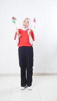 Happy Asian girl celebrate Indonesia independence day in red and white outfit holding a rose and tiny Indonesia flag isolated on white background photo