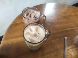 Tabletop shot A pair of cold drinks. A cold chocolate drink next to a cold vanilla drink served with a large glass held on a brown wooden table. Tasty Beverage with Text space photo