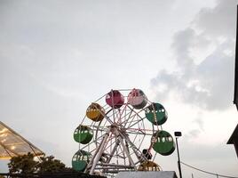 A mini Ferris wheel with a sunset sky in the background. The gondolas, or cabins, of the Ferris wheel are brightly colored. An amusement ride on the rooftop of a shopping center. Ads space. photo