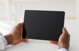 Technology for treat. Unrecognizable african american doctor using digital tablet with blank screen, empty space, mockup for ad. Male therapist sitting at workplace in office, closeup, crop photo