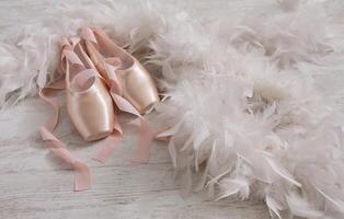 Pastel pink ballet shoes background. New pointe shoes with satin ribbon lay on white rustic shubby chic wood near feather boa, view with copy space photo