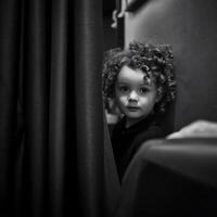 A Child's Curious Gaze from Behind a Curtain Black and White Portrait. photo