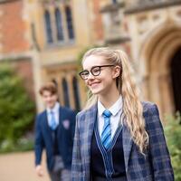 Happy Teenage Girl in School Uniform Walking on Campus. A cheerful young woman smiles while walking past a blurred background of a historic school building. photo