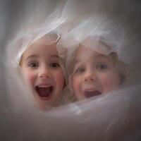 Two Happy Children Peek Through Sheer Fabric. A close up image of two joyful toddlers playfully hidden behind a delicate, white textile. photo