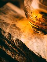 Amber Liquid in Glass on Rough Stone Surface. Close up of a golden beverage resting on textured rocks. photo