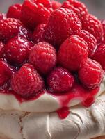 Close up of a Pavlova dessert topped with fresh raspberries and raspberry sauce. photo