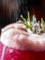 Close up of a pink bubbly drink with rosemary garnish, water droplets falling. photo