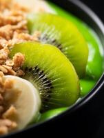 Close up of a vibrant green smoothie bowl topped with kiwi slices, banana, and granola. photo