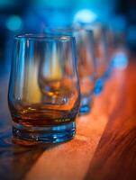Close up of glasses of amber liquid on a wooden surface with blurred background lighting. photo