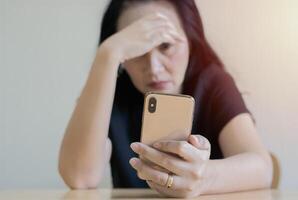 Sad woman sitting at the table with smartphone and worried with problem at home. photo